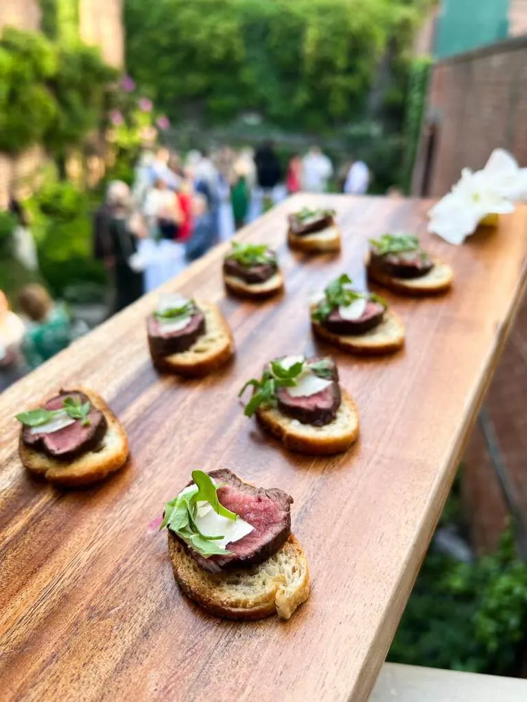 Seared beef crostini on a wooden board at an outdoor garden event