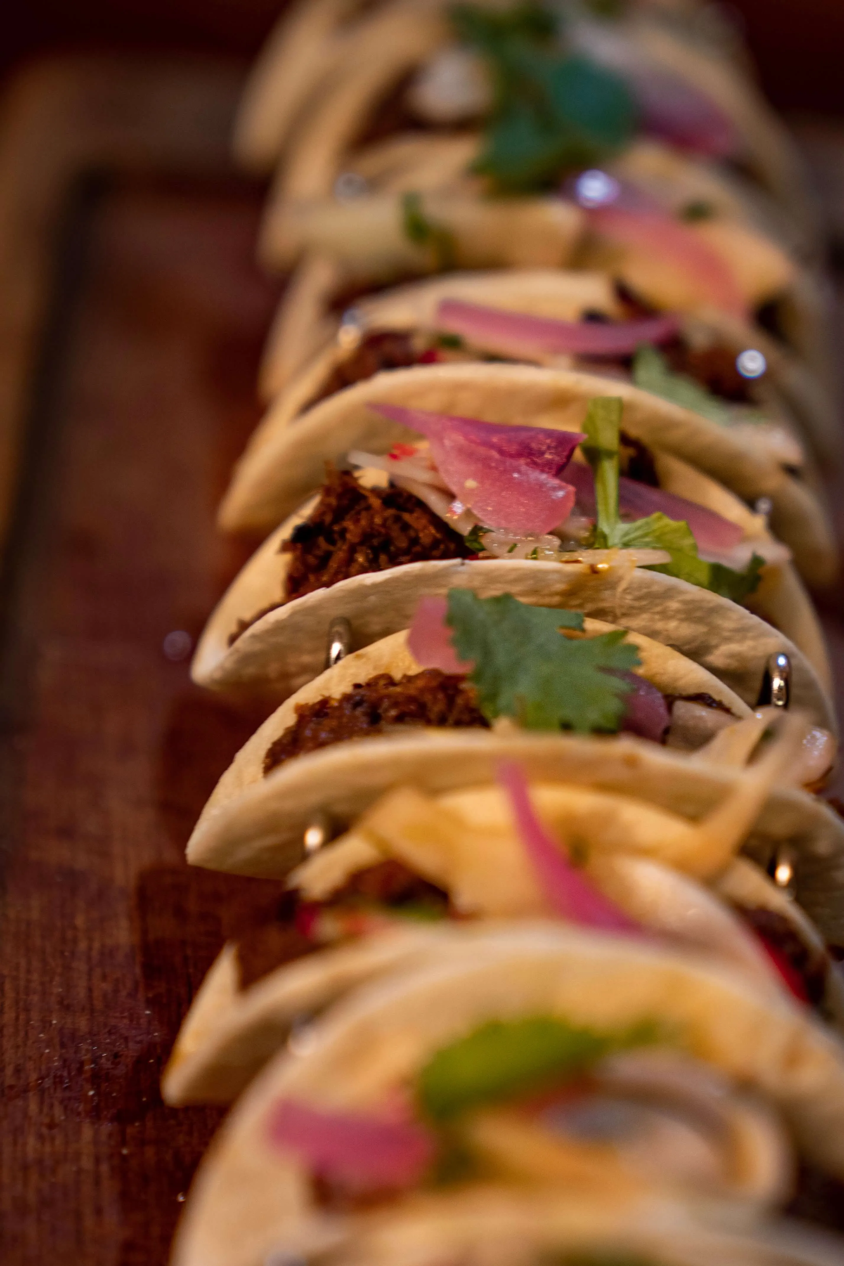 Row of soft tacos topped with cilantro and pickled onion