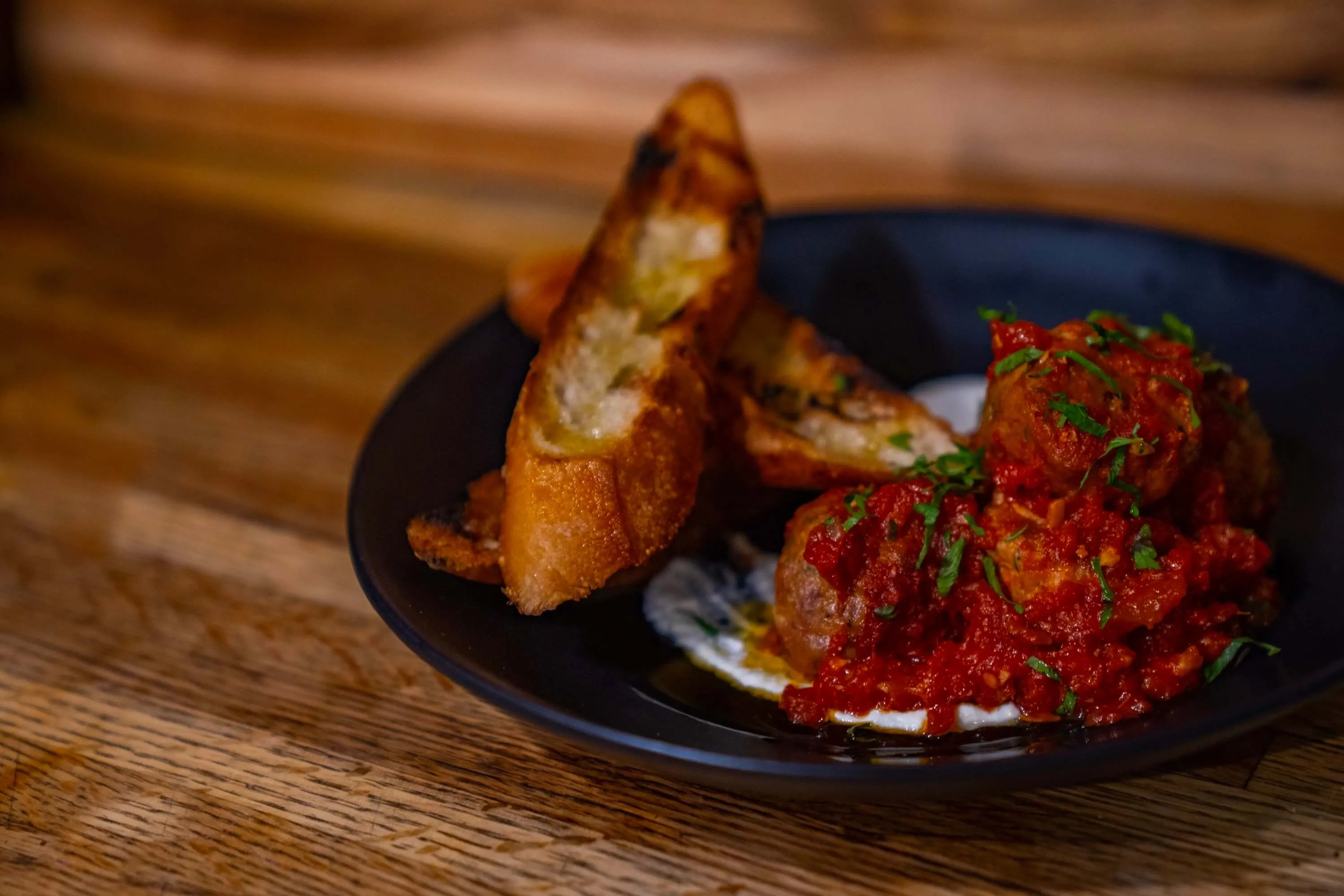 Mini meatballs in marinara with grilled crostini in a black bowl