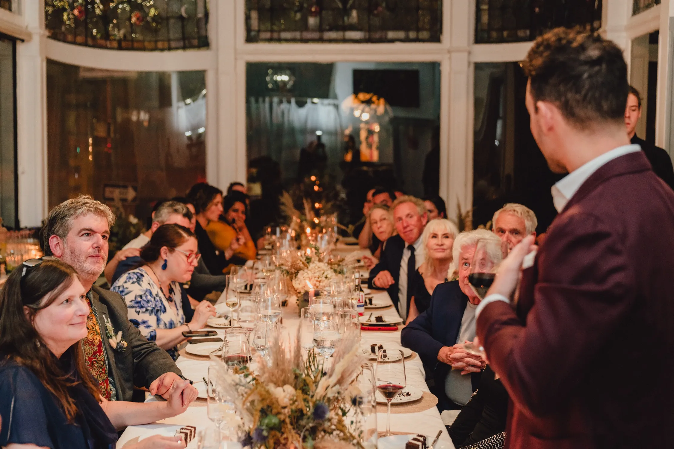 Guests seated at a long candlelit dinner during a toast