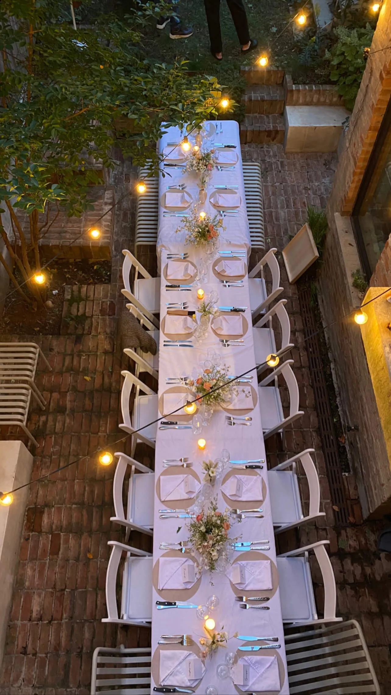 Long banquet table set with linens, flowers, and candles in a backyard