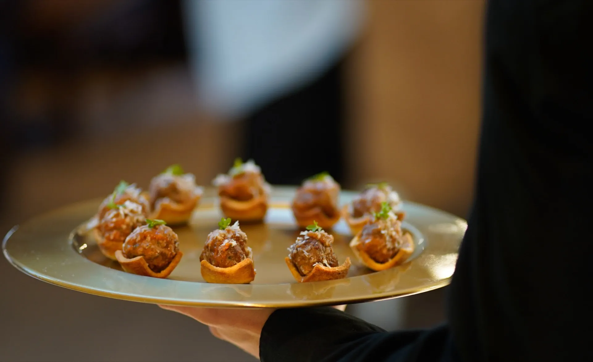 Server holding a gold tray of meatball crostini cups