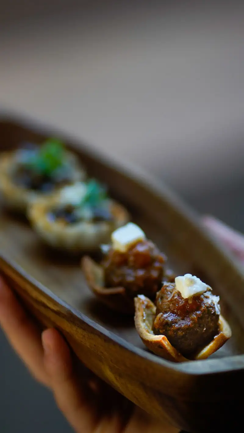 Hand holding a wooden tray of meatball and mushroom canapés