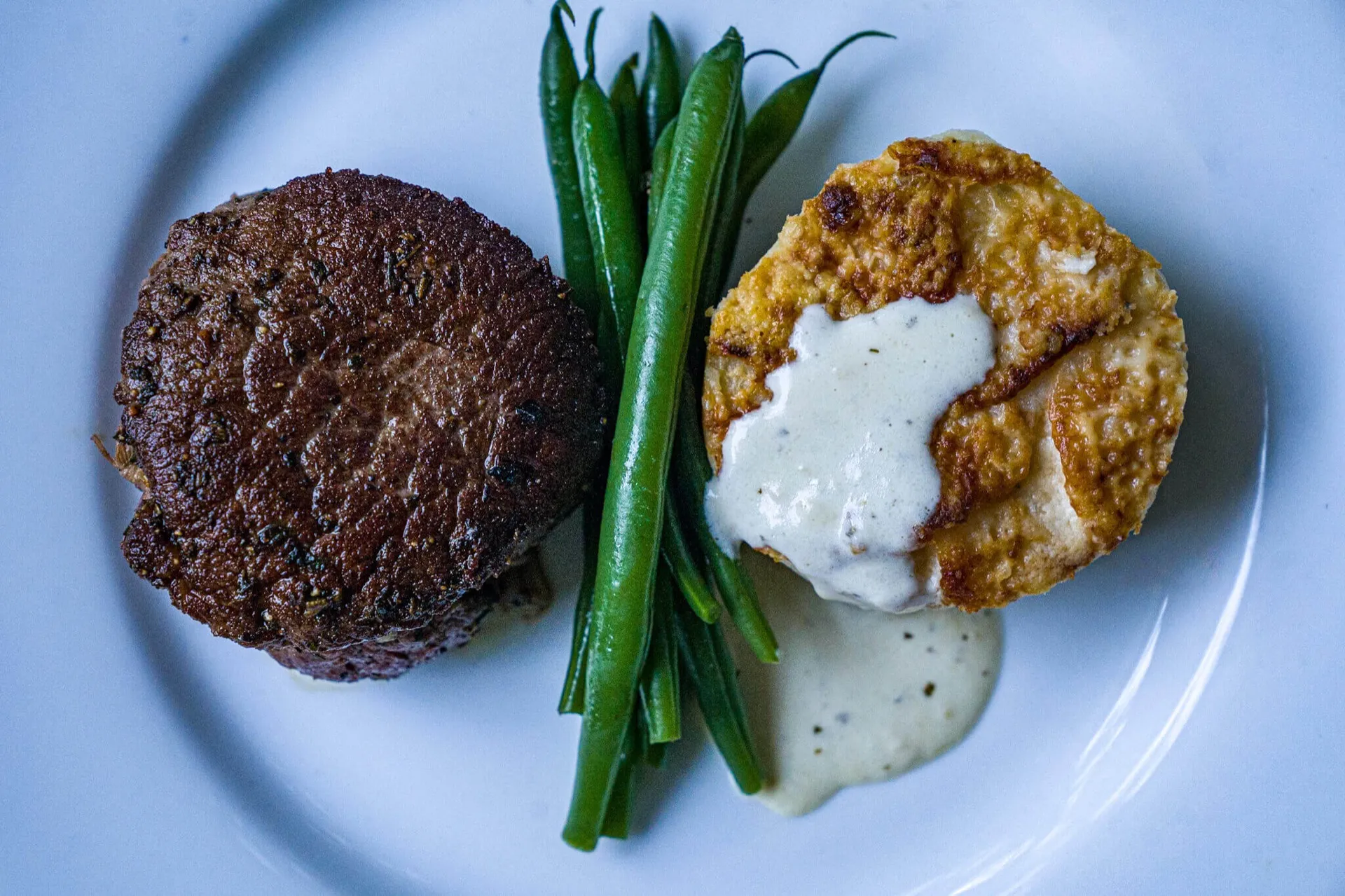 Plated filet mignon with green beans and crab cake in cream sauce