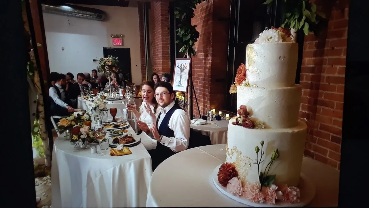 Bride and groom at the head table beside a floral tiered wedding cake