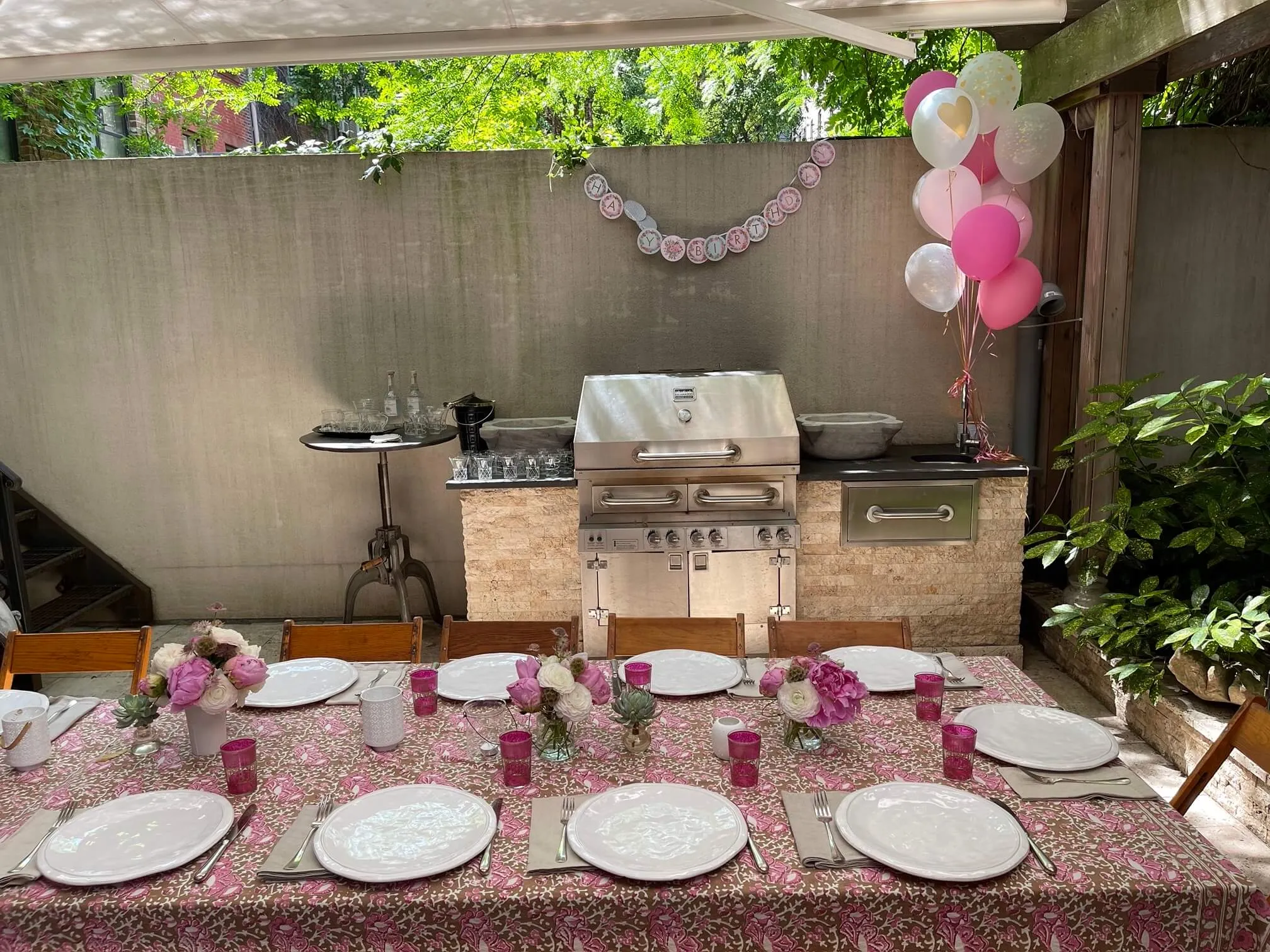 Patio birthday table set with pink linens beside a grill and balloons