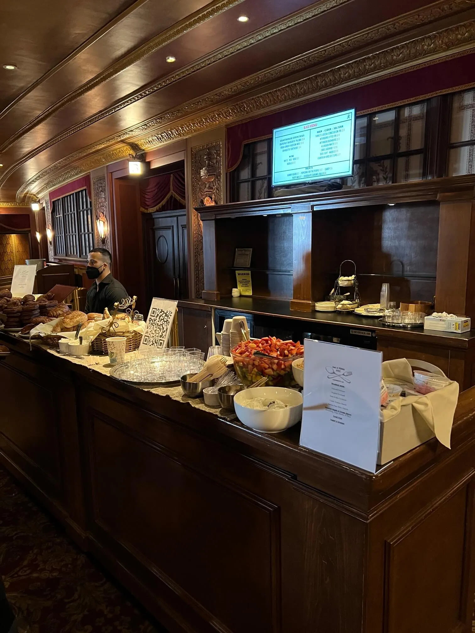 Server behind a breakfast buffet of pastries and fruit salad