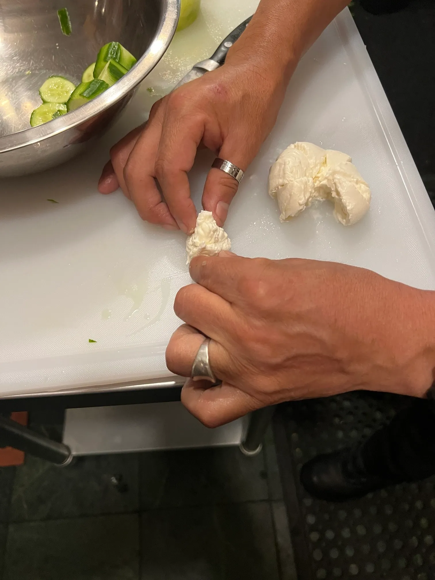 Chef pulling fresh mozzarella by hand beside sliced cucumbers