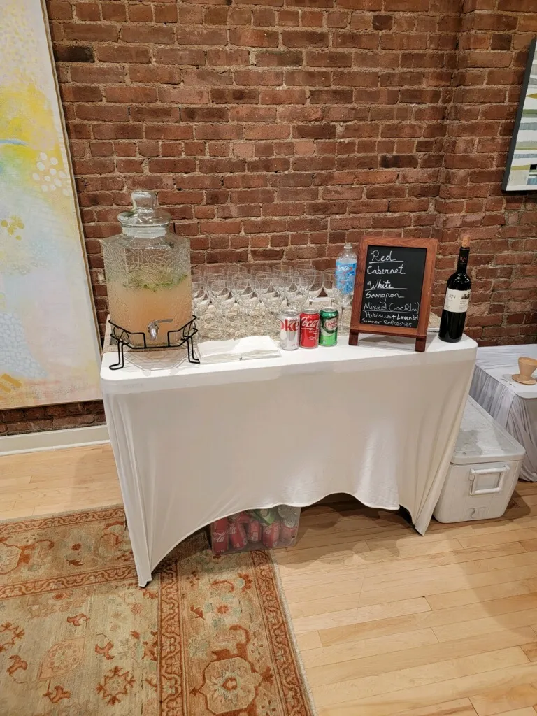 Self-serve beverage table with lemonade, wine, and sodas by exposed brick