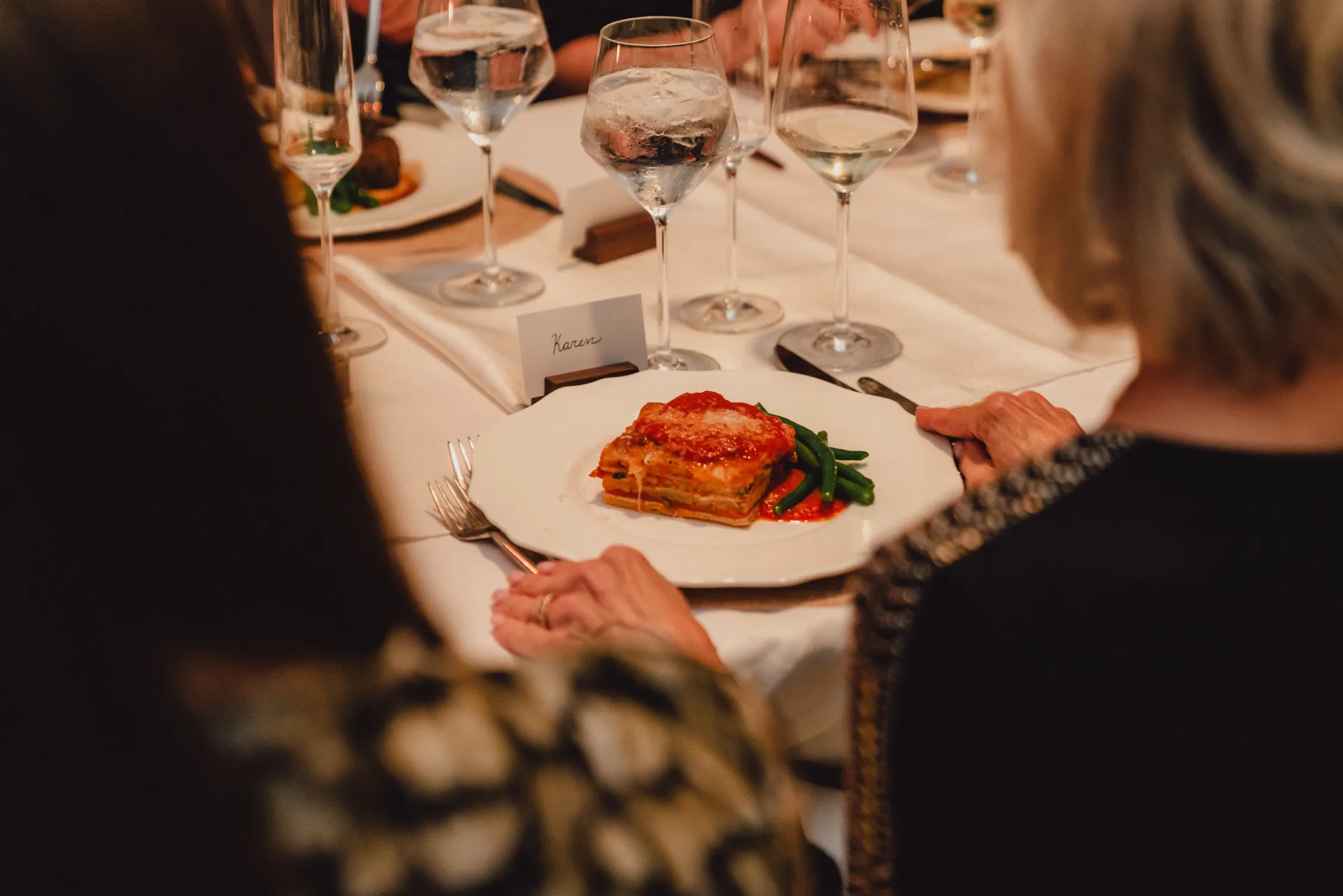 Guest served a plated slice of lasagna and green beans at a candlelit dinner
