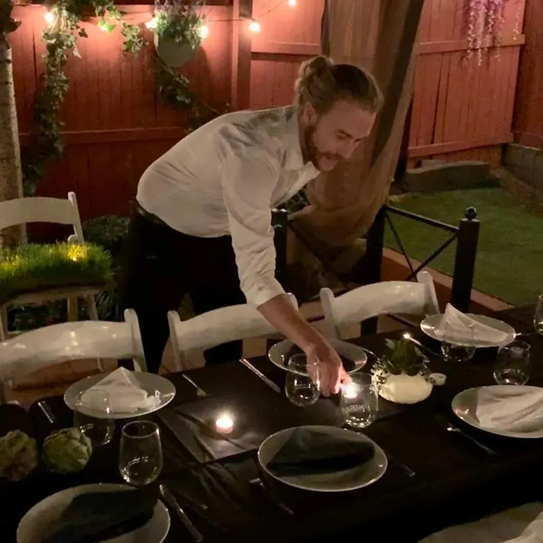 Server lighting candles on a set backyard dinner table at night
