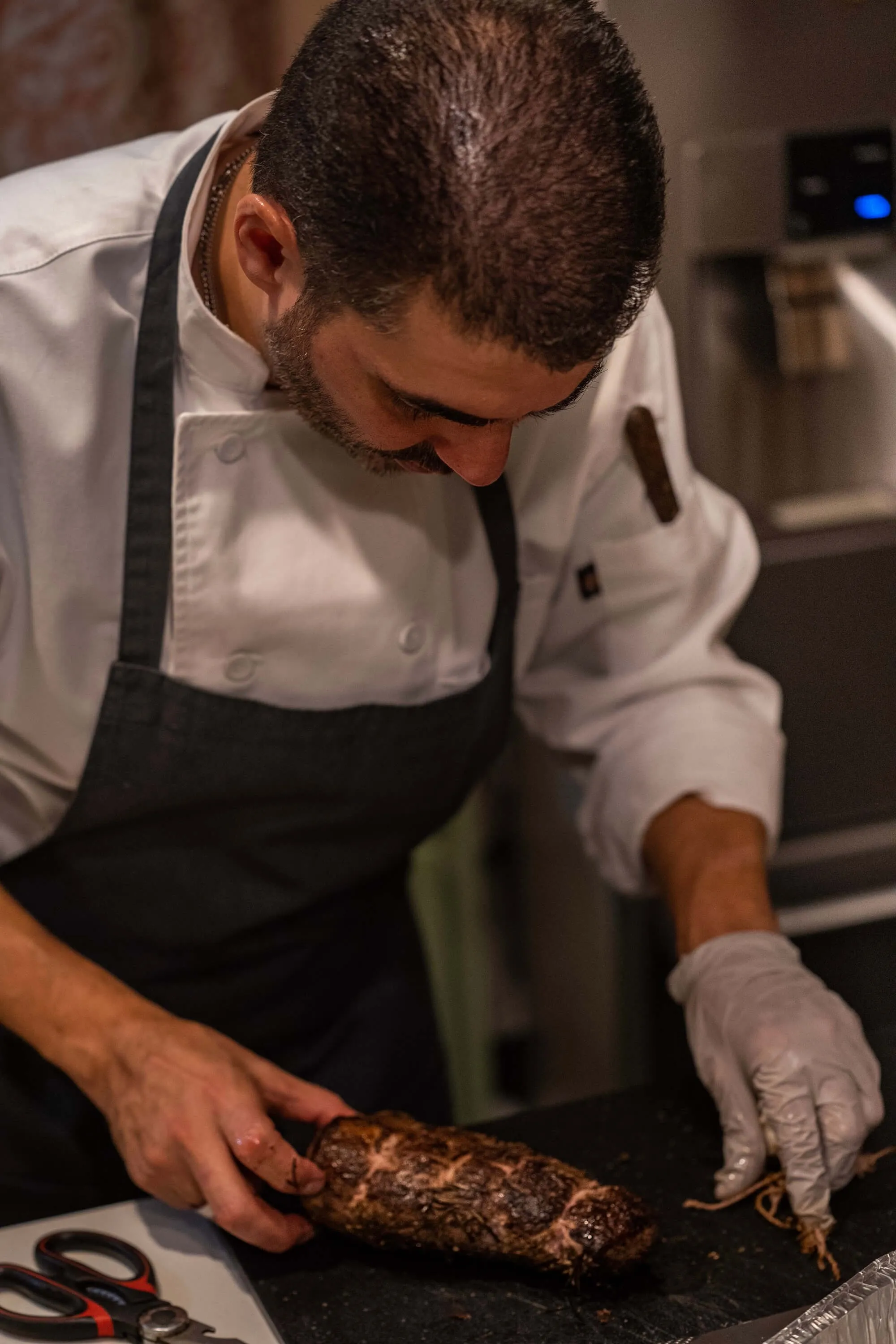 Chef in an apron trussing a seared roast on a kitchen counter